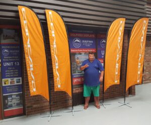 Four orange feather flags on cross bases in front of a storefront window