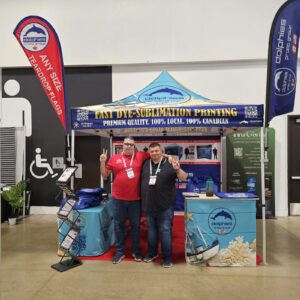 Teardrop flag and feather flag on either side of a trade show booth with a printed canopy tent and table cover