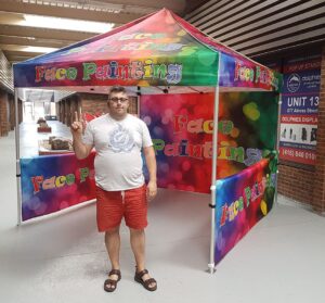 Pop-up tent with a multicoloured printed canopy, a printed back wall and a side wall, indoors