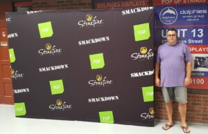 Man beside a black step-and-repeat 10 ft pop up fabric display with green logos