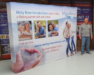Man beside a white 10 ft pop up fabric display with photos of couples, angled view