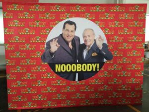 Red step-and-repeat 10 ft pop up fabric display with a round photo of two men