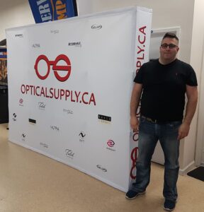 Man beside a white 10 ft pop up fabric display with a red glasses logo, angled view
