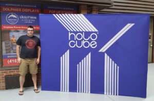 Man beside a blue 10 ft pop up fabric display with large white lettering