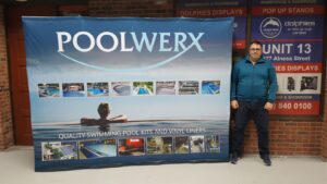Man beside a blue 10 ft pop up fabric display with a swimming pool photo