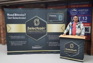 Man at a black printed counter in front of a dark 10 ft pop up fabric display with a gold coin graphic