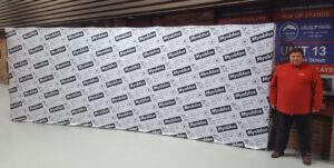 Man beside a white step-and-repeat 20 ft pop up fabric display with black logos