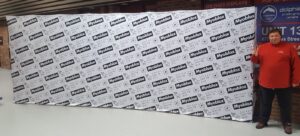 Man beside a white step-and-repeat 20 ft pop up fabric display with black logos, wide view