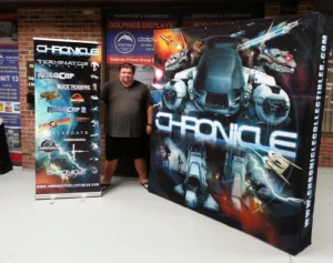 Man beside a black 8 ft pop up fabric display with a robot illustration, next to a roll-up banner