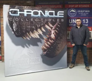 Man beside a grey 8 ft pop up fabric display with a dinosaur skull image