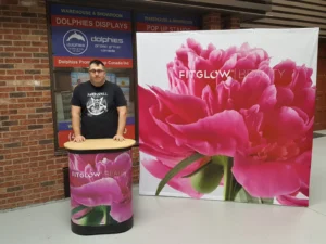 Man at a matching printed counter in front of an 8 ft pop up fabric display with a pink flower photo