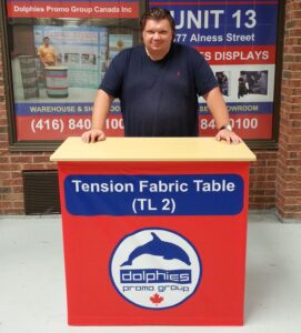 Man behind a red pop up fabric counter with a blue header and a dolphin logo