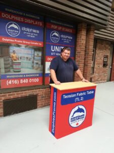 Man beside a red pop up fabric counter, side view showing the printed end