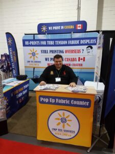 Man sitting behind a yellow pop up fabric counter at a trade show booth