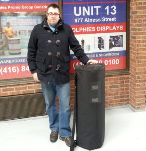 Man standing with the pop up fabric counter packed in its black carrying bag, side view