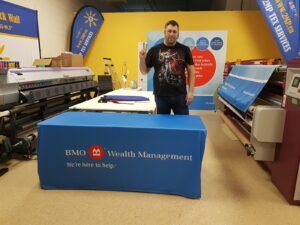 Blue fitted table cover with a white and red logo in the print shop