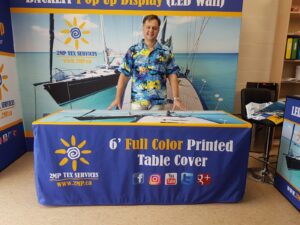 Blue fitted table cover with a printed top in front of a pop up display