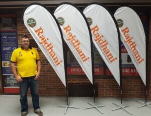 Four white custom printed teardrop flags with orange lettering on cross bases