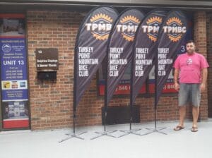 Four black custom printed teardrop flags with orange logos on cross bases