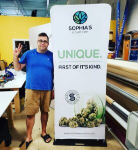 Man beside a 3 ft tube fabric display with a white graphic and green leaf logo in the print shop