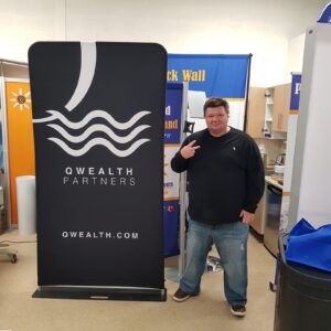 Man beside a black a 3 ft tube fabric display with a white wave logo