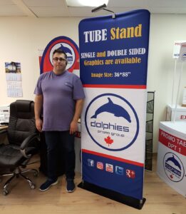 Man beside a 3 ft tube fabric display with a blue dolphin logo graphic