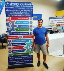 Man beside a 3 ft tube fabric display with a blue graphic listing industries