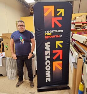 Man beside a black a 3 ft tube fabric display with orange and red arrows