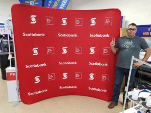 Man beside a red step-and-repeat an 8 ft curved tube fabric display with white logos