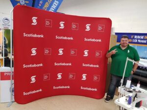 Another view of a red step-and-repeat an 8 ft curved tube fabric display with a man beside it