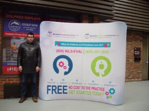 Man beside a white an 8 ft curved tube fabric display with colourful icons and green text