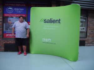 Man beside a green an 8 ft curved tube fabric display with a white logo