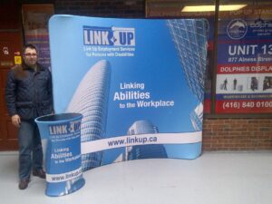 Man beside a blue an 8 ft curved tube fabric display with a matching round printed counter
