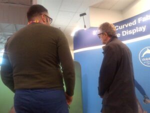 Two men talking beside curved tube displays at a trade show